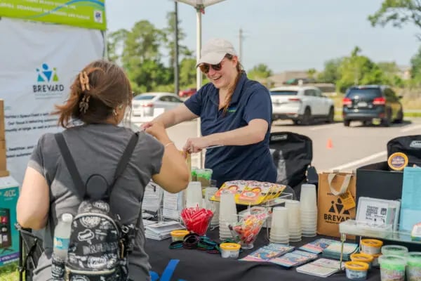 woman standing behind table passes out information at booth
