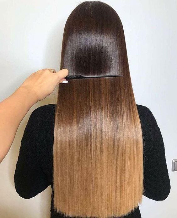 Estilista peinando cabello largo, lacio y brillante con un degradado balayage de castaño a rubio.