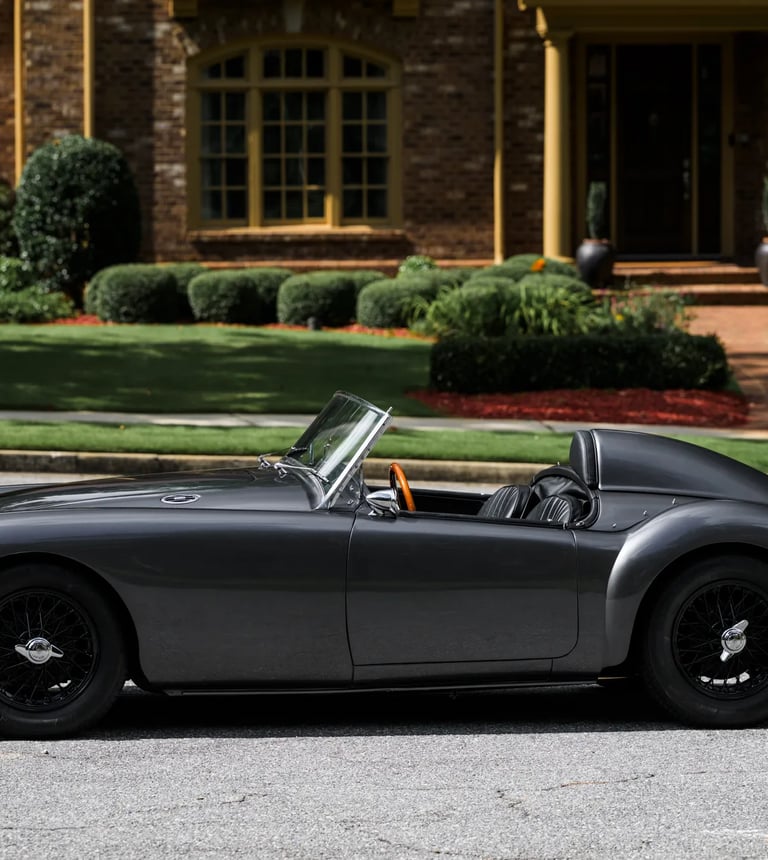 A photo of a 1958 MG MGA Roadster in a garden setting.