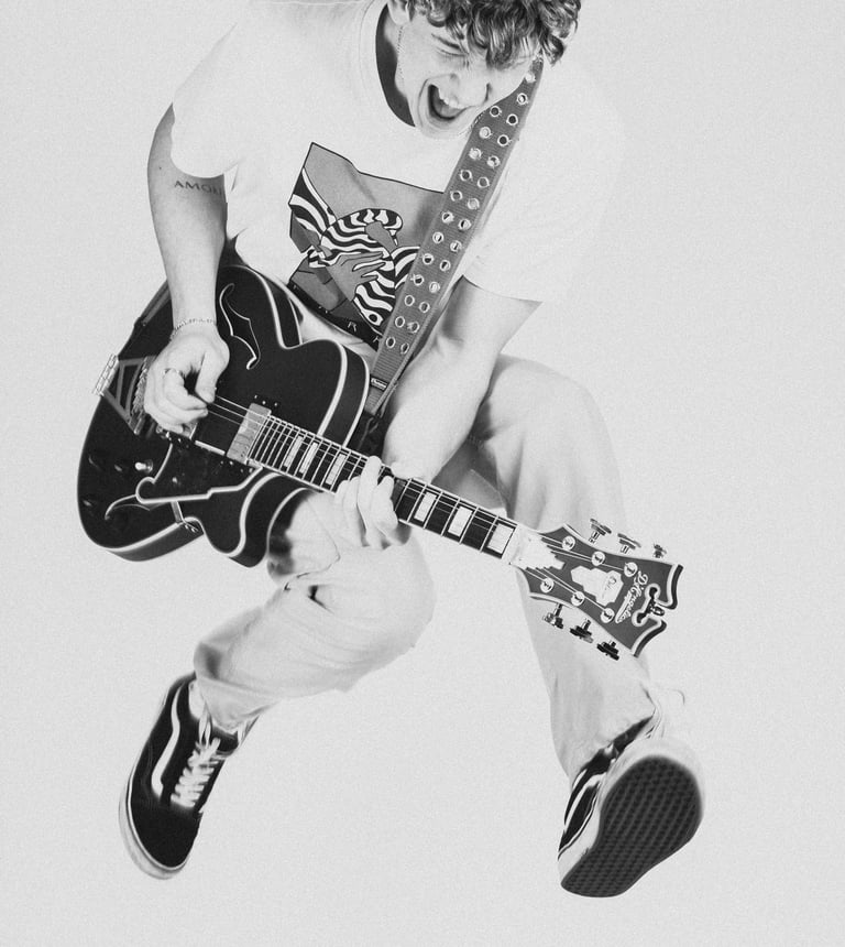 portrait of a man jumping in a white shirt and tie dye on a guitar