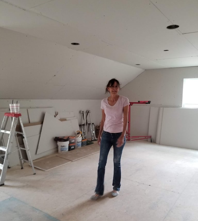Janestands in a room under construction featuring newly installed drywall and home renovation tools.