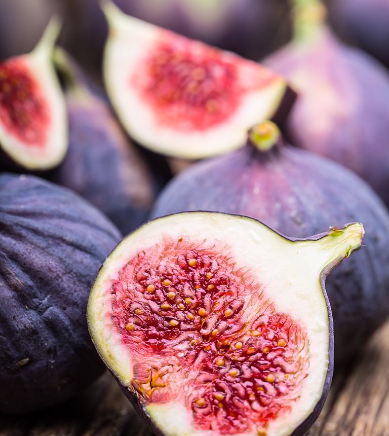 Fresh ripe purple figs sliced open showing a sweet red interior on a rustic wooden table.
