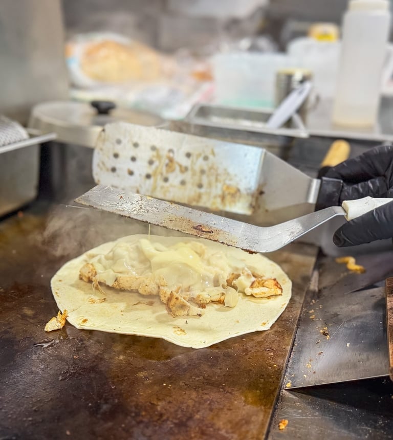 Chef grilling a chicken quesadilla with melted cheese on a flat top commercial griddle.