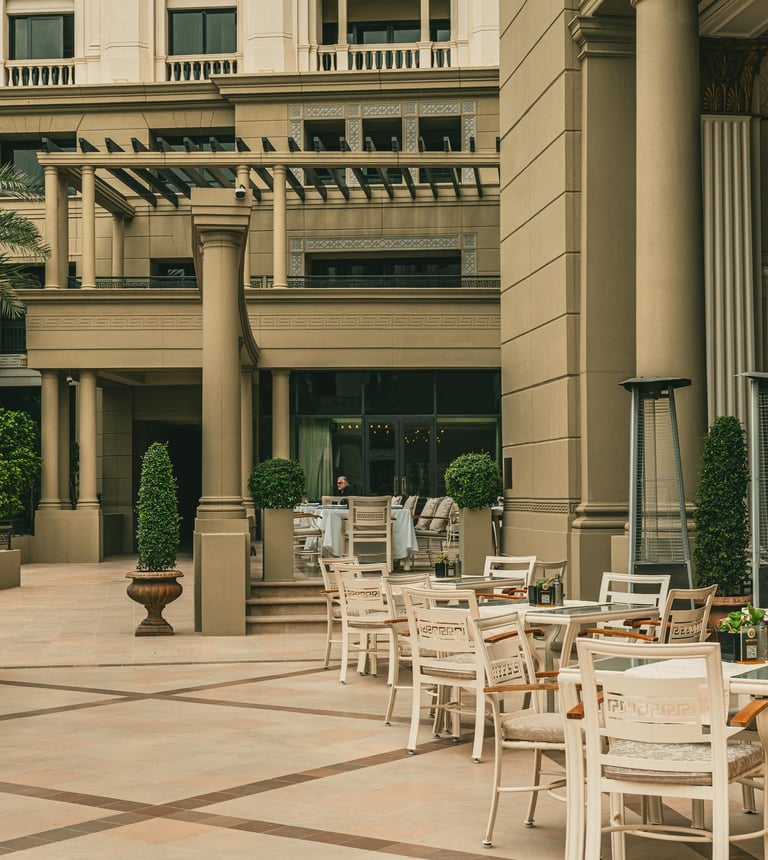 Elegant outdoor patio seating at a luxury hotel with white chairs and classical architecture.