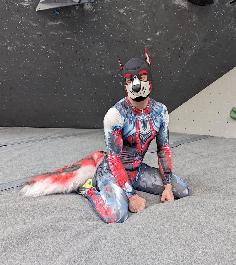 Man kneeling in bodysuit and pup mask.