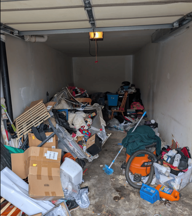 Deep Garage overfilled with a variety of items including pallets, outdoor toys, boxes, and furniture
