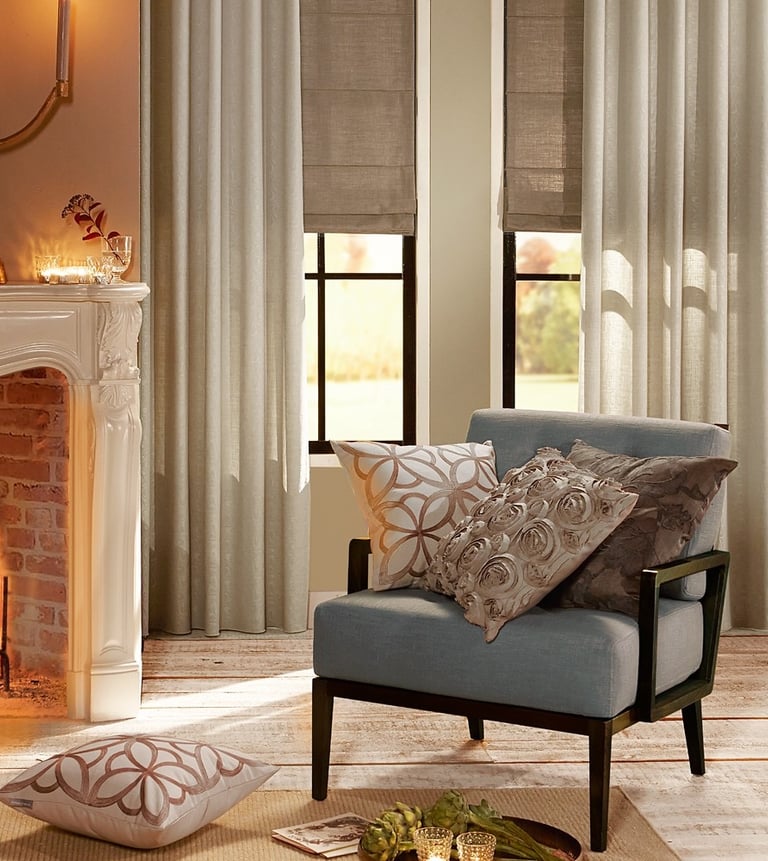 Elegant living room with beige linen curtains, roman shades, and a blue armchair by a fireplace.