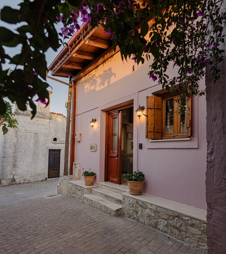 Charming cottage entrance: soft pink exterior, wooden doors, vibrant purple flowers