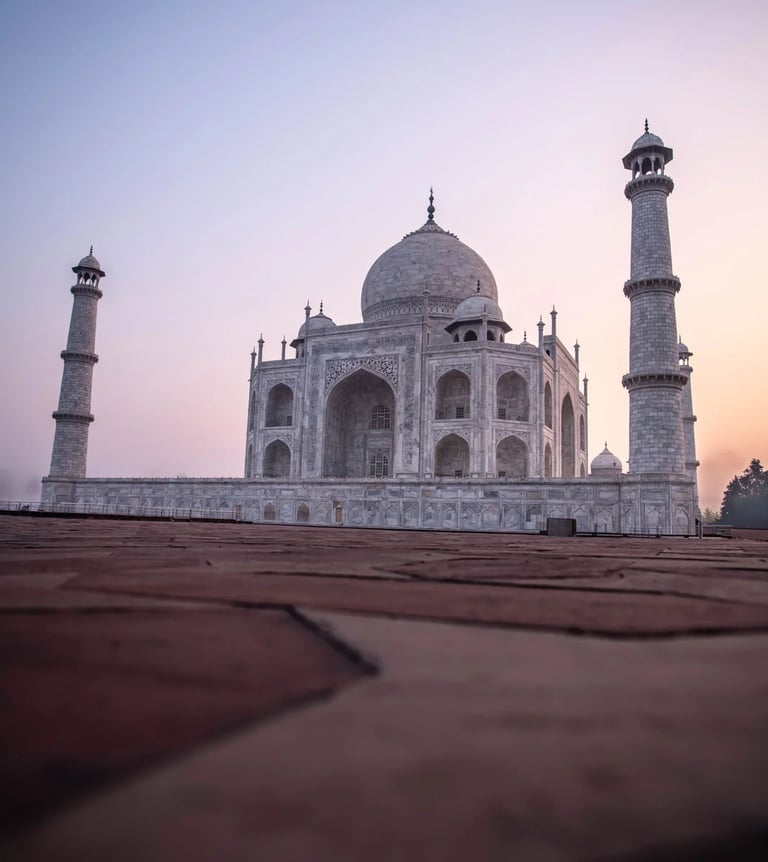 Low angle view of the Taj Mahal in Agra at sunrise with white marble domes and minarets.