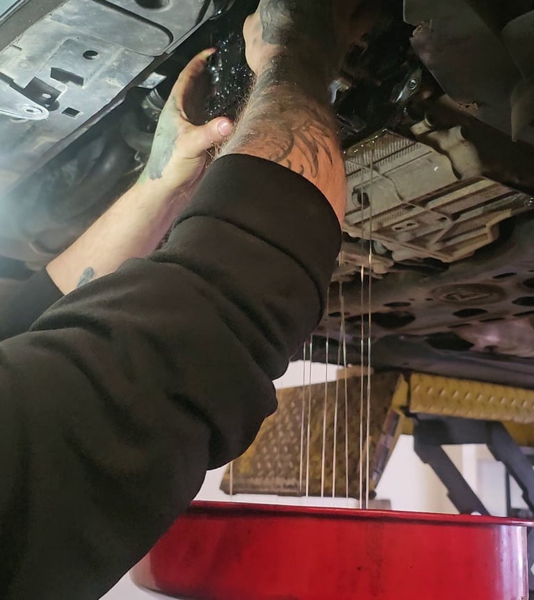 Mechanic draining old oil into a red collection pan during a mechatronic repair