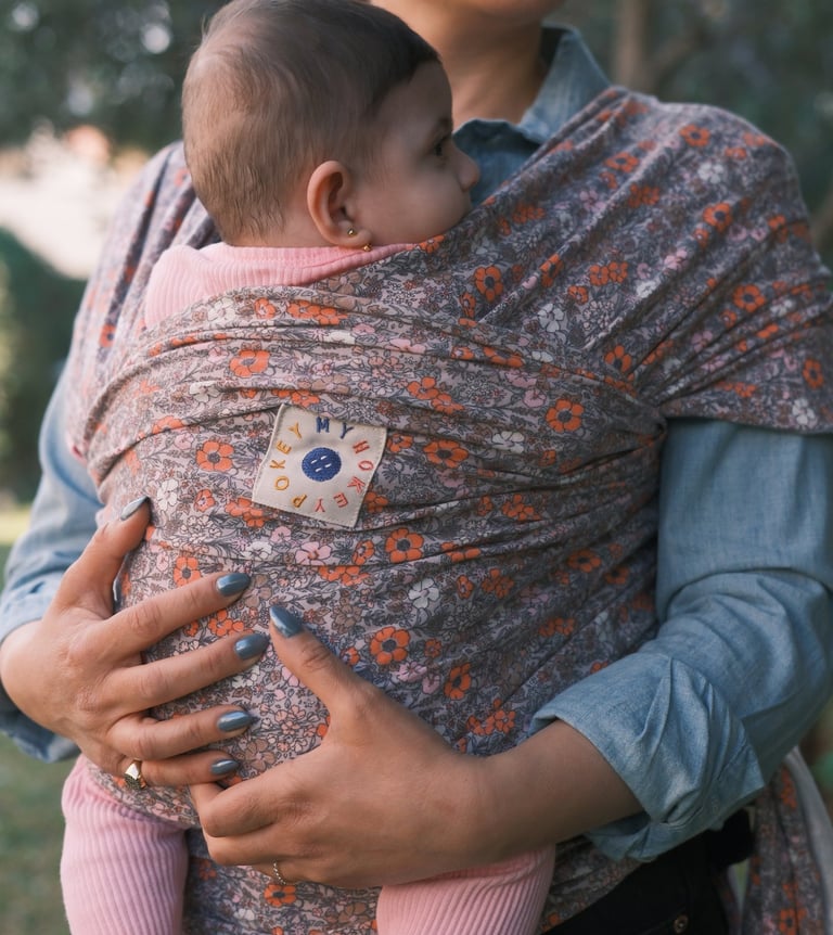 Mother holding her baby in a floral patterned ergonomic baby wrap carrier outdoors.