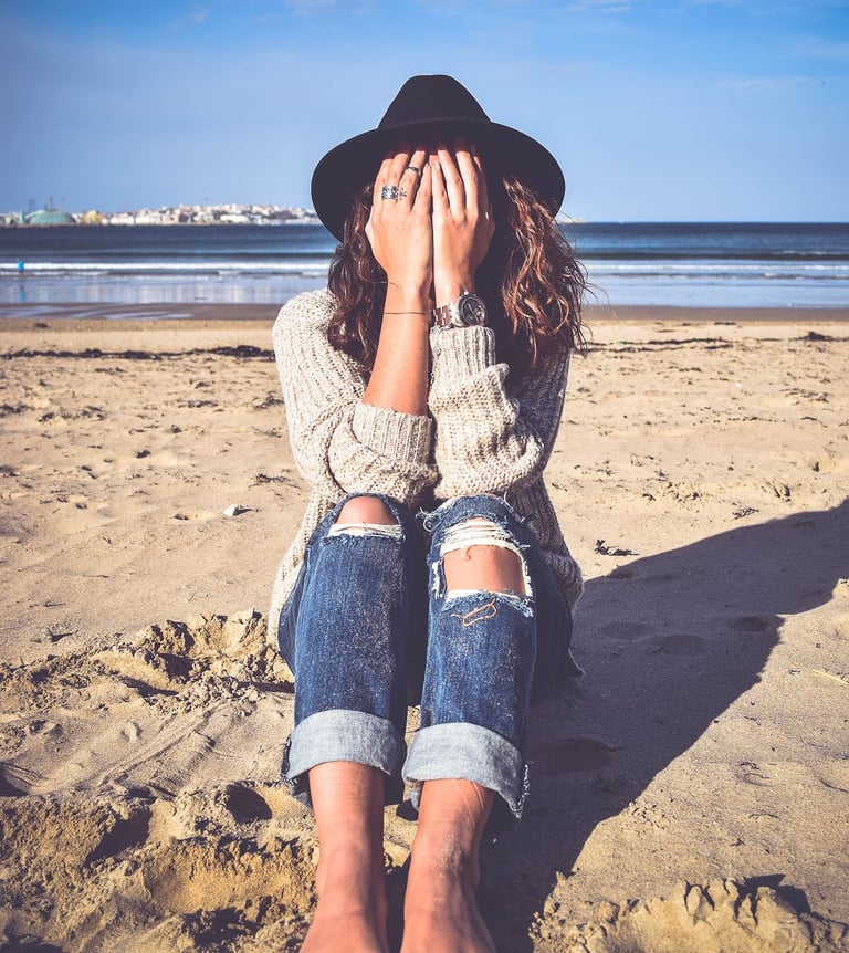 une femme qui se cache les yeux assise sur le sable