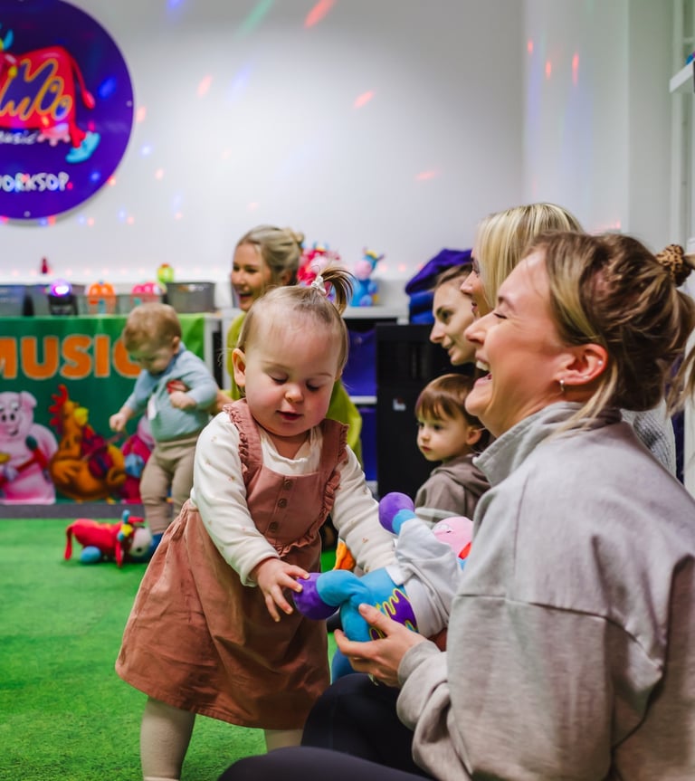 A young Mini Moo attendee and her Mum smiling and laughing, playing with a soft toy.