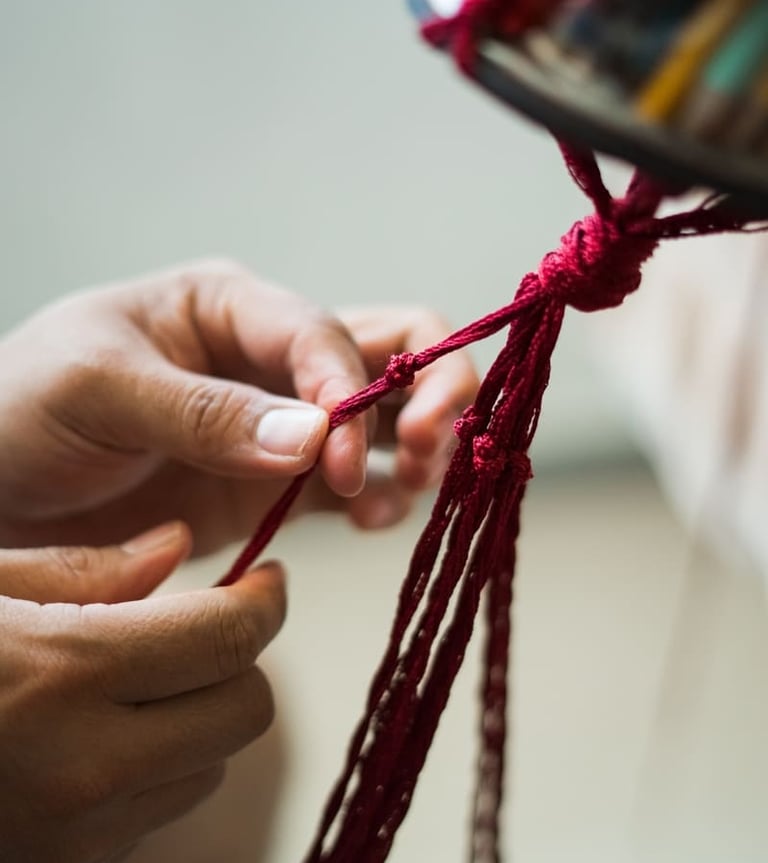 Manos haciendo un nudo decorativo con hilo rojo intenso para un proyecto textil artesanal.