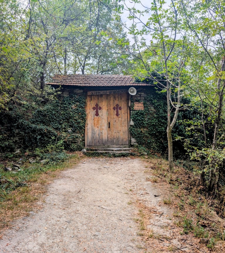Monastery of Saint Nikola with wooden doors and red crosses tucked into a green ivy-covered forest.