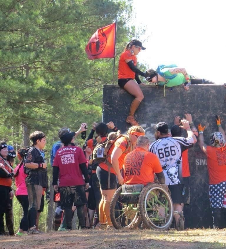 people helping other athletes over a wall at a spartan race