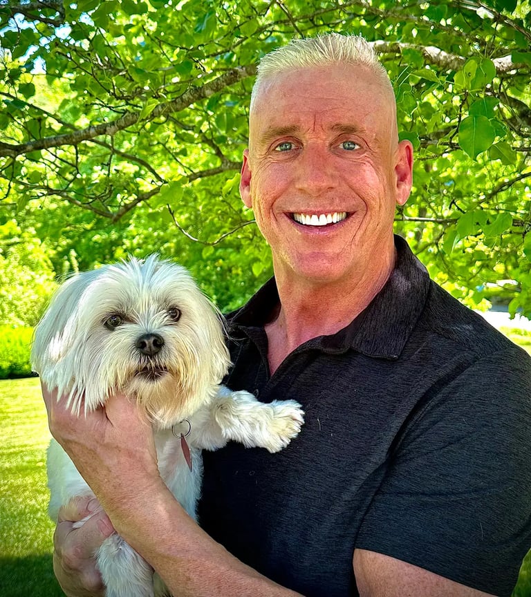 a man in a black shirt is holding a white dog; Tom O'Brien, Owner, Tymeless Properties