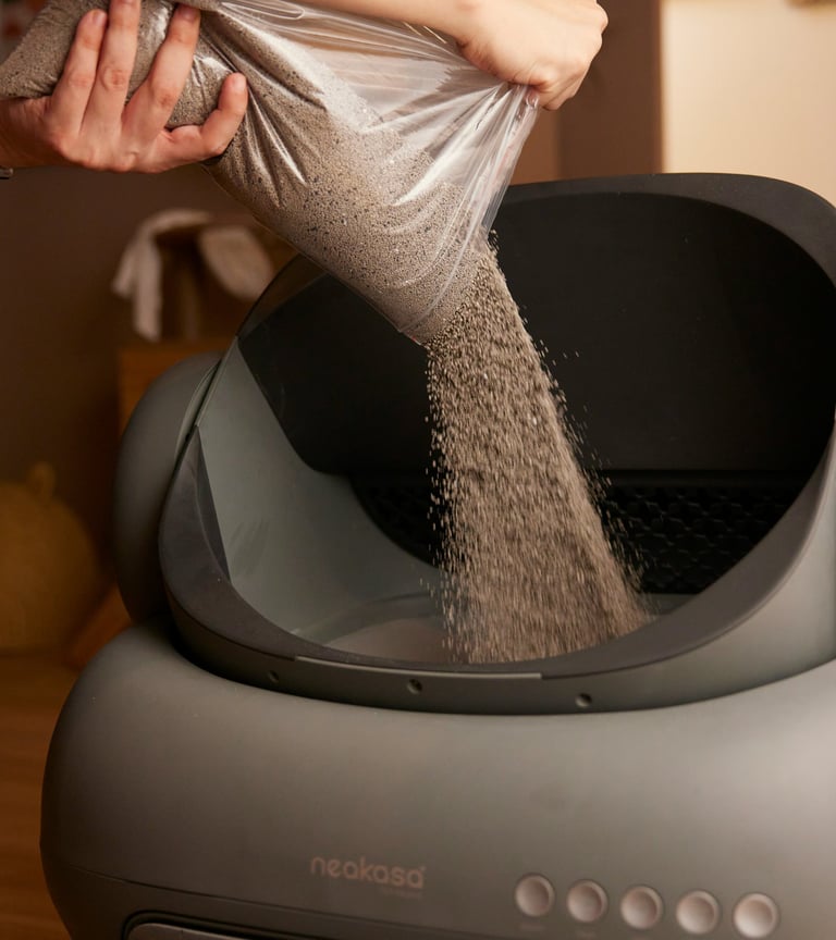 A person pours fresh clumping litter from a bag into an automatic self-cleaning Neakasa cat litter box.