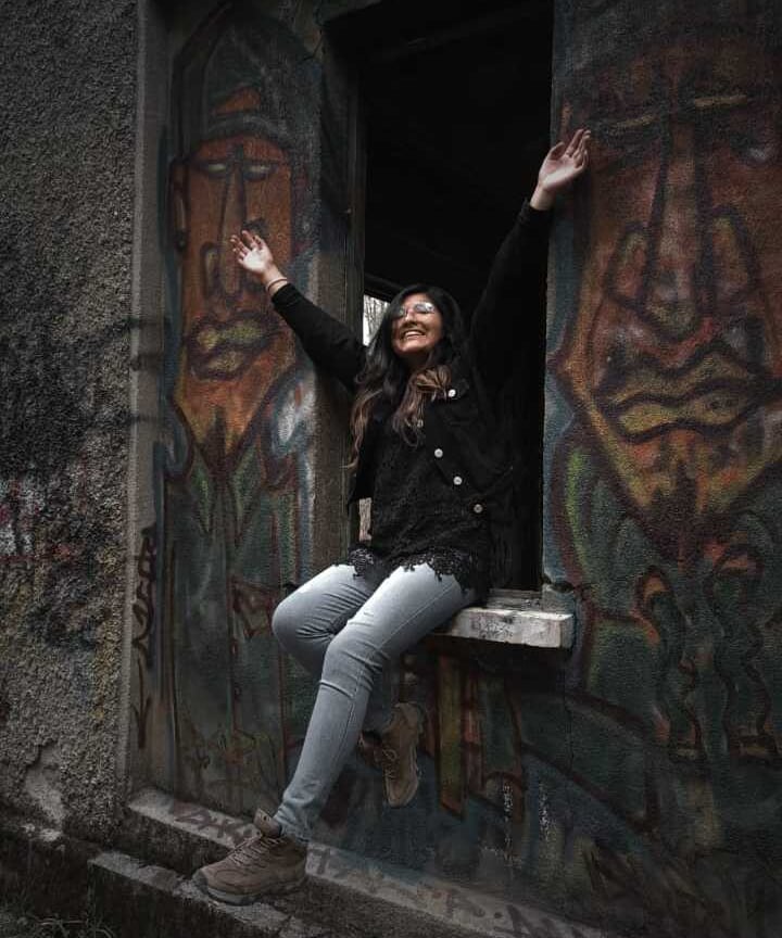 Una mujer sonriente sentada en la ventana de un edificio abandonado, rodeada de arte de grafiti
