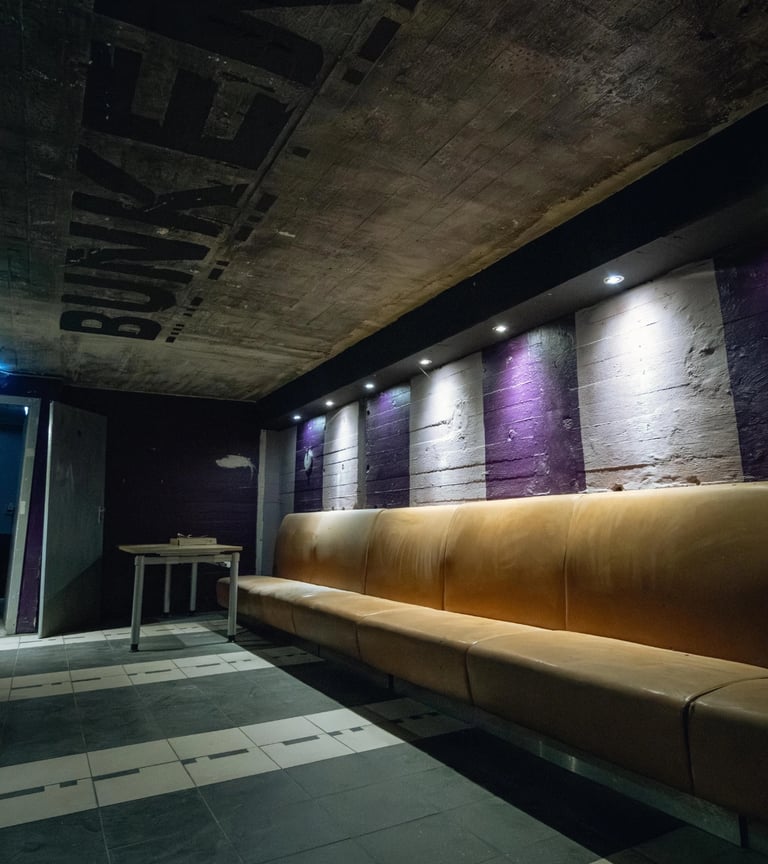 Long leather bench in an underground bunker lounge with industrial concrete walls and purple accents.
