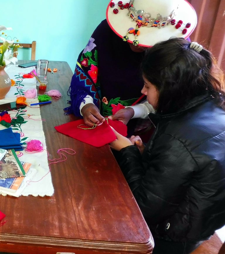 turistas y artesanas bordando juntas sentadas alrededor de una mesa