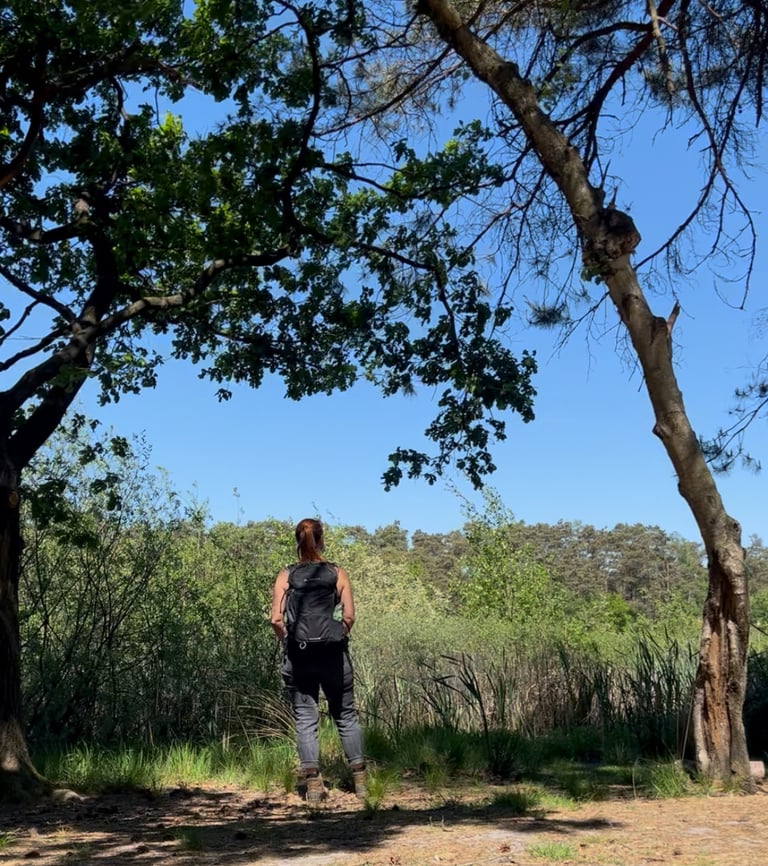 Anneke met rugzak, uitkijkend over een vijver, omringd door bomen