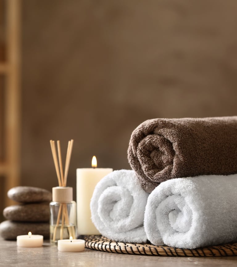 Rolled spa towels, candles, and essential oils arranged in a calming wellness setting