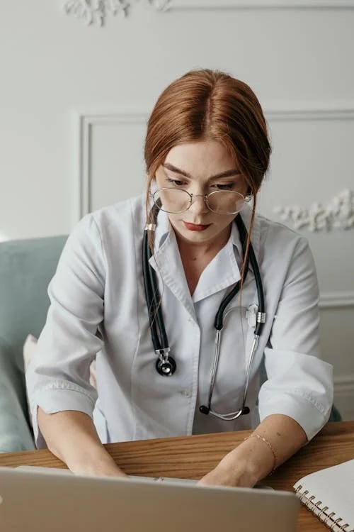 a woman in a white lab coat and glasses is sitting at a desk with a