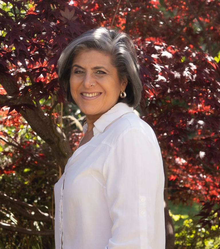 Smiling woman with short salt and pepper hair posing in front of a red Japanese maple tree.