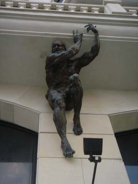 Bronze muscular male statue mounted to a stone wall as an architectural feature on a building facade.