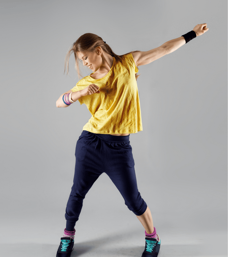 Una donna che danza con energia, indossando una maglietta gialla, pantaloni blu scuro e scarpe sportive nere con dettagli tur