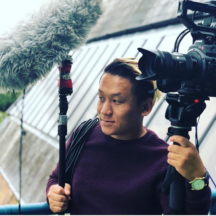 a man in a purple sweater holding a microphone and a video camera