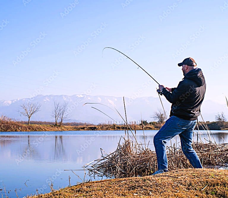 homem pescando tucunaré a beira do lago com vegetação seca ao chao e montanha ao fundo