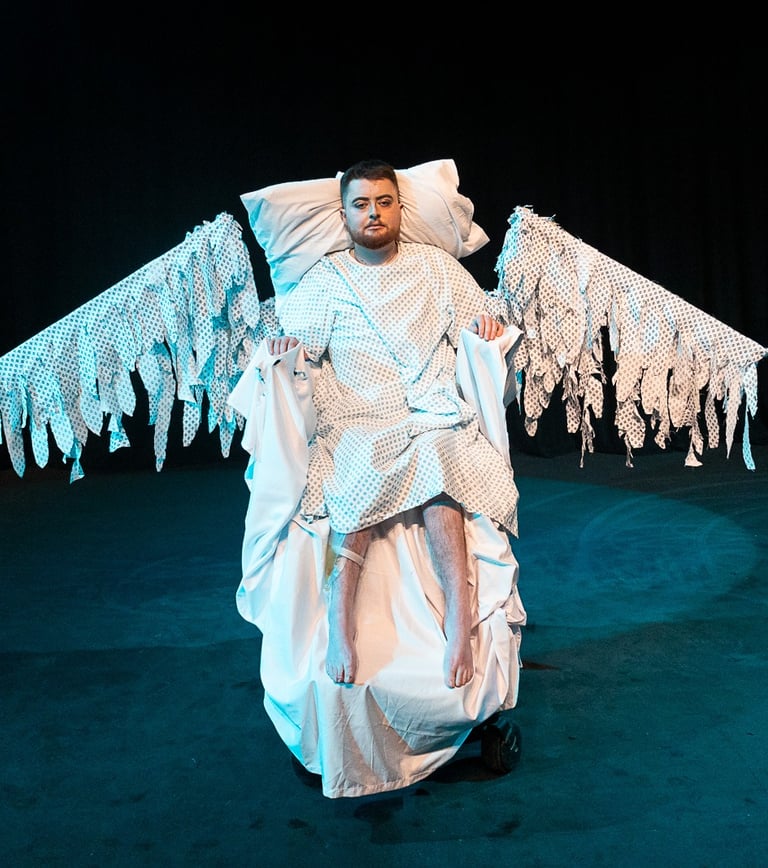 Jamie Hale sits in an electric wheelchair made up like a bed, hospital gown wings splayed out wide