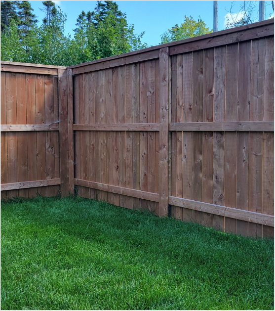 A brown cedar wood privacy fence bordering a lush green backyard lawn with trees in the background.