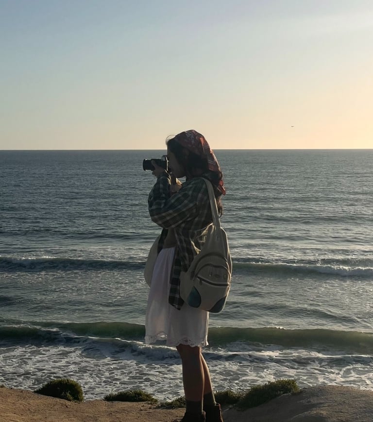 Vibey full body candid shot of me holding camera up to my face, standing on cliffs over ocean.Earthy