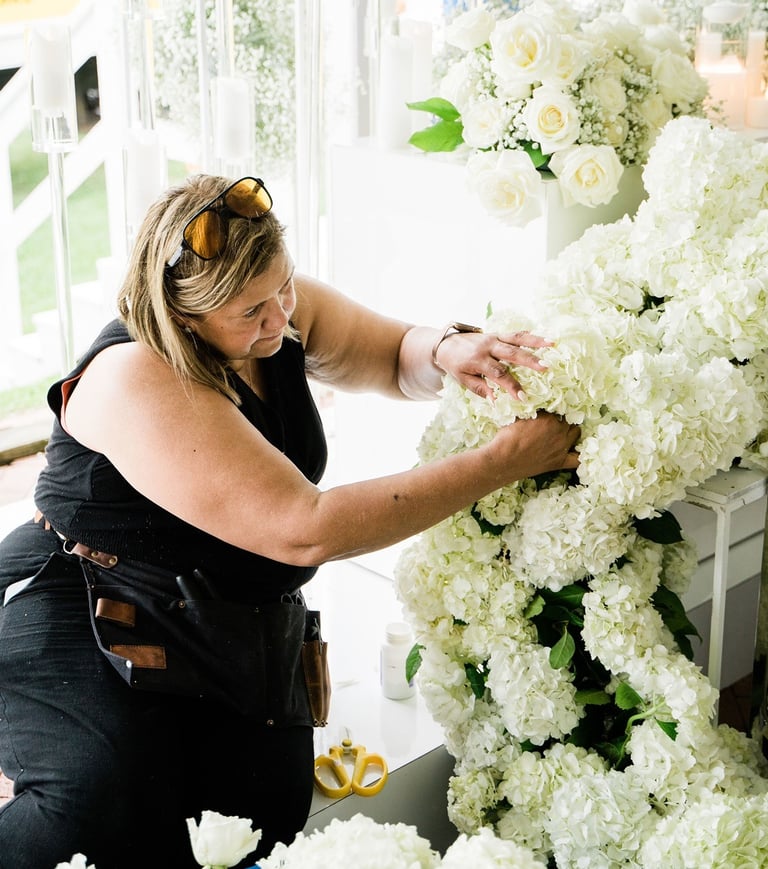 a woman in a black dress is standing in front of a large flower arrangement