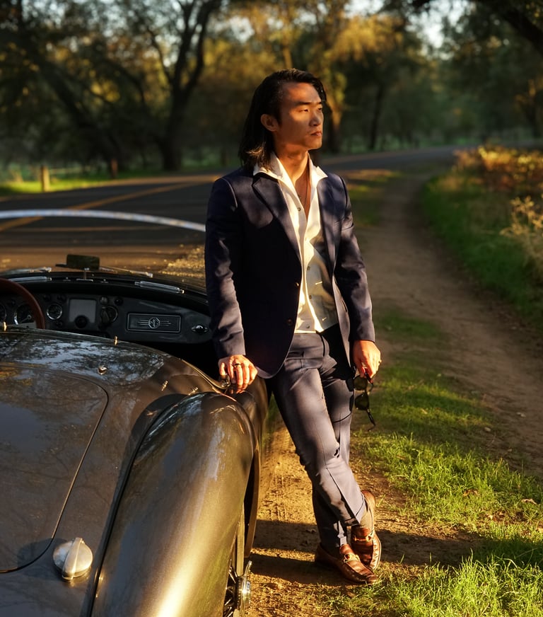 A man leaning against the passenger side of a 1958 MG MGA Roadster in a park during golden hour.