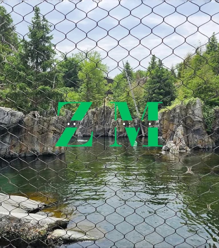 Stainless steel zoo mesh fence protecting a naturalistic animal enclosure with water and rocks.
