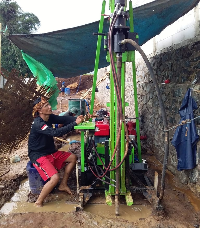 Technician operating a portable hydraulic water well drilling rig at an outdoor construction site.