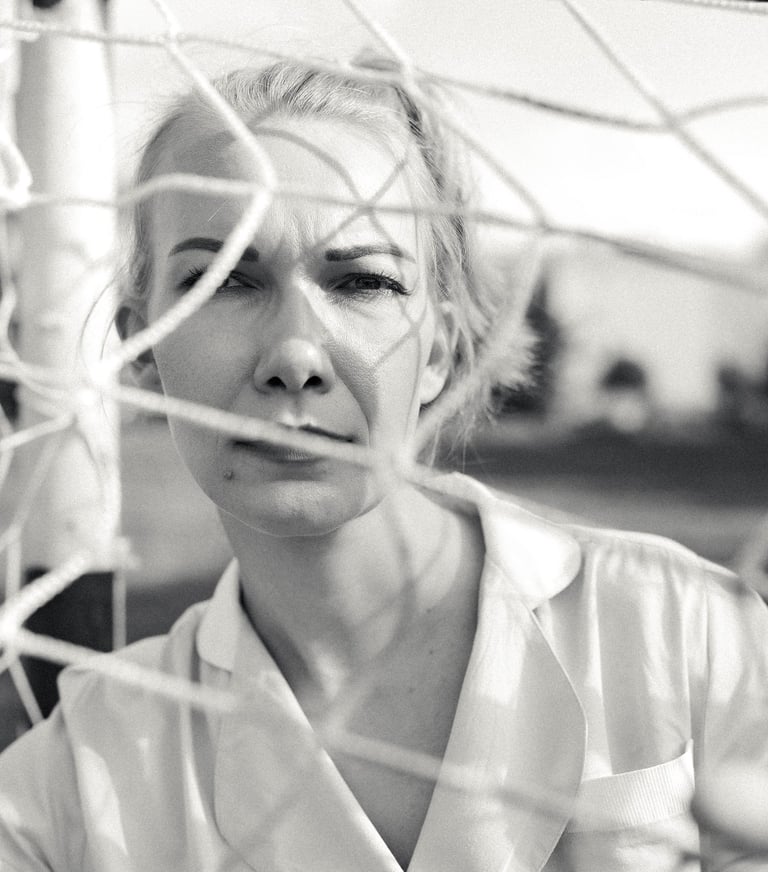 Black and white portrait of a woman looking through a soccer goal net on a field.
