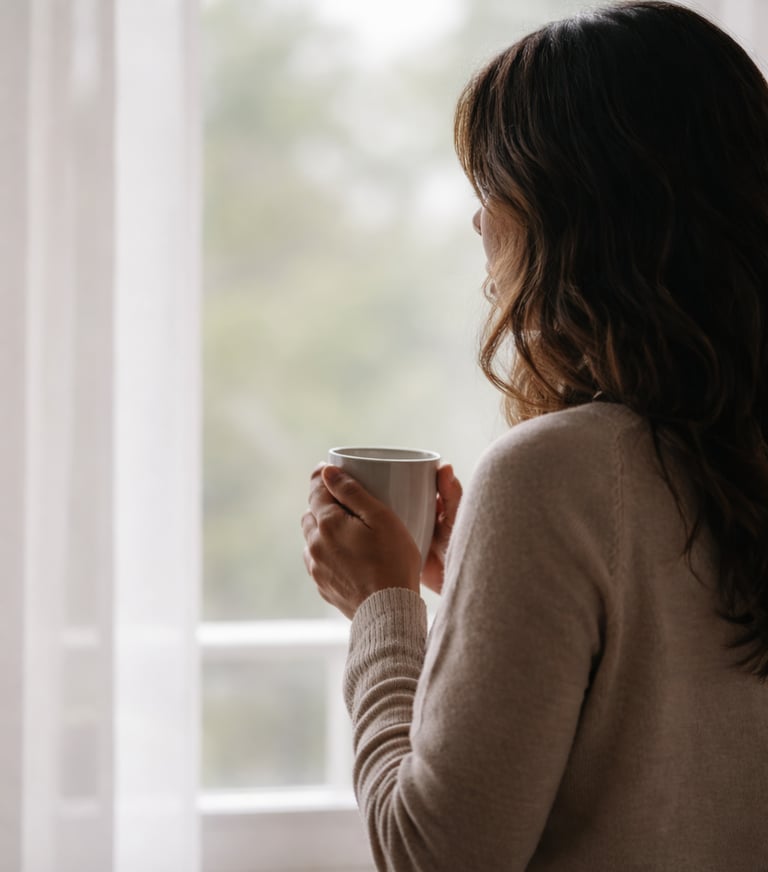 Silueta de mujer mirando por la ventana con una taza de té después de haber perdido su trabajo.