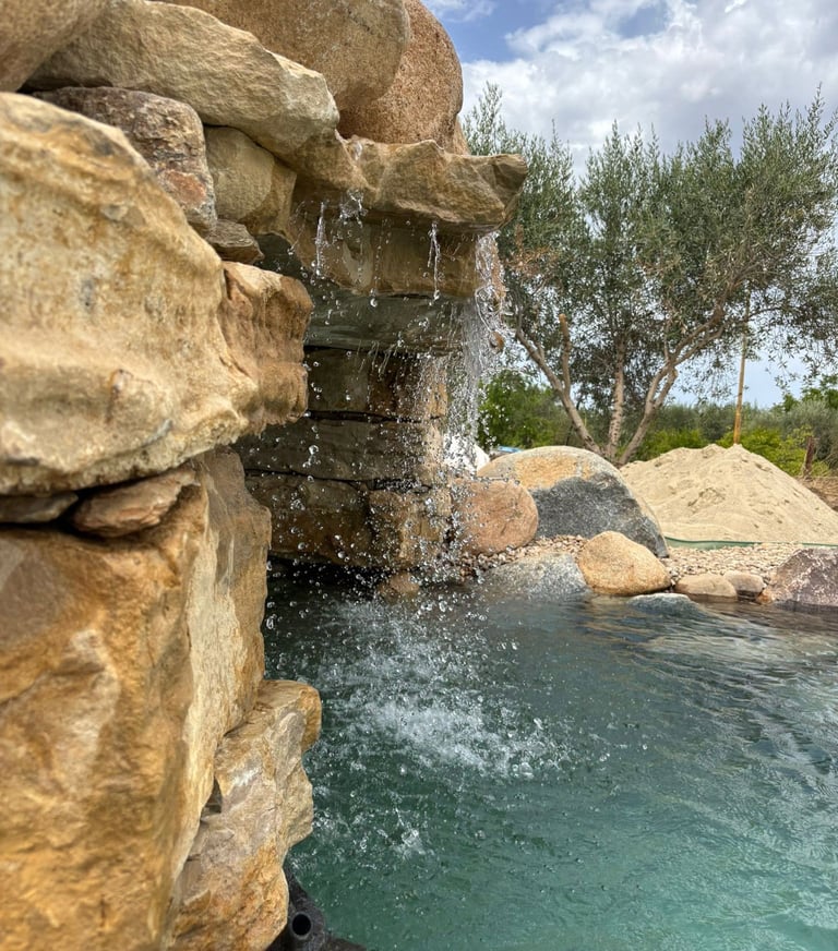 Piscina effetto spiaggia con cascata e area relax outdoor