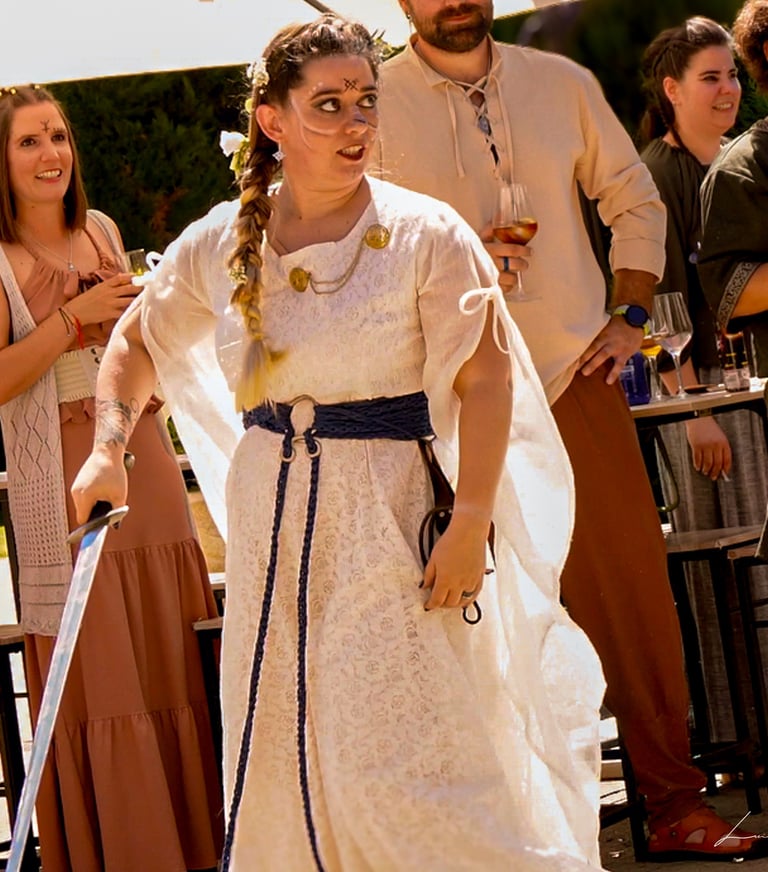 Mujer con vestido blanco y cinturón azul empuñando una espada durante una ceremonia de boda medieval