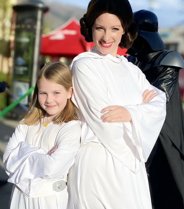 A young girl and woman in Princess Leia costumes pose with Darth Vader at a Star Wars event.