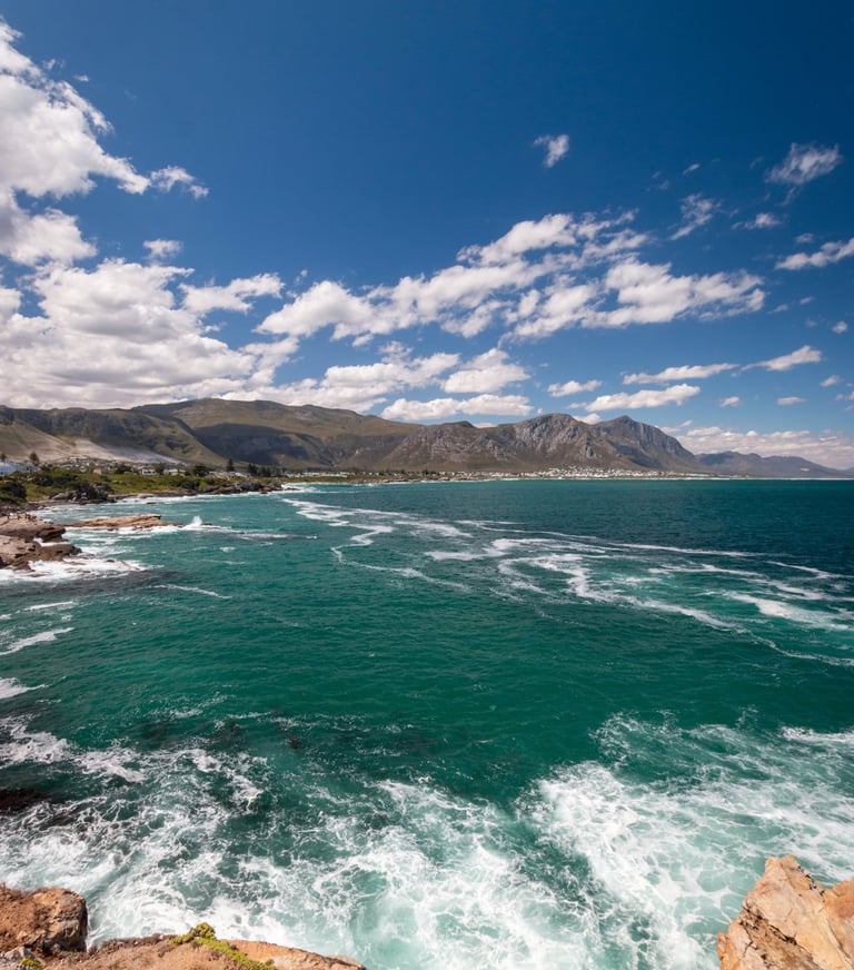 Scenic coastal landscape featuring turquoise ocean waves crashing against rocky cliffs under a bright blue sky.