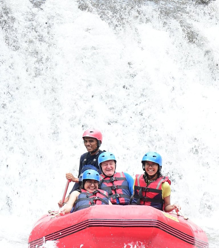 Smiling group in life jackets white water rafting on a splashing river waterfall.
