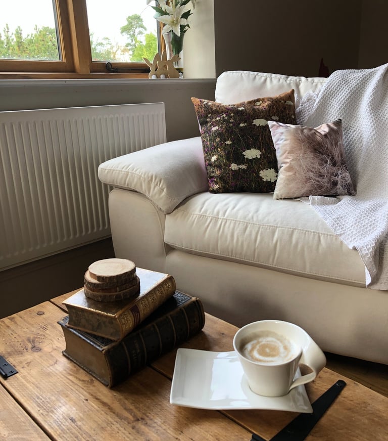 a cosy living room with cushions, a cup of coffee and a stack of books