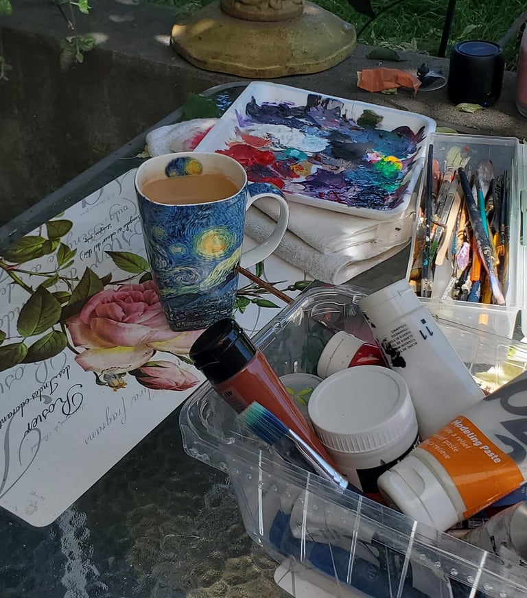 A photo of an artist's desk with all the necessary tools to paint including a big cup of coffee