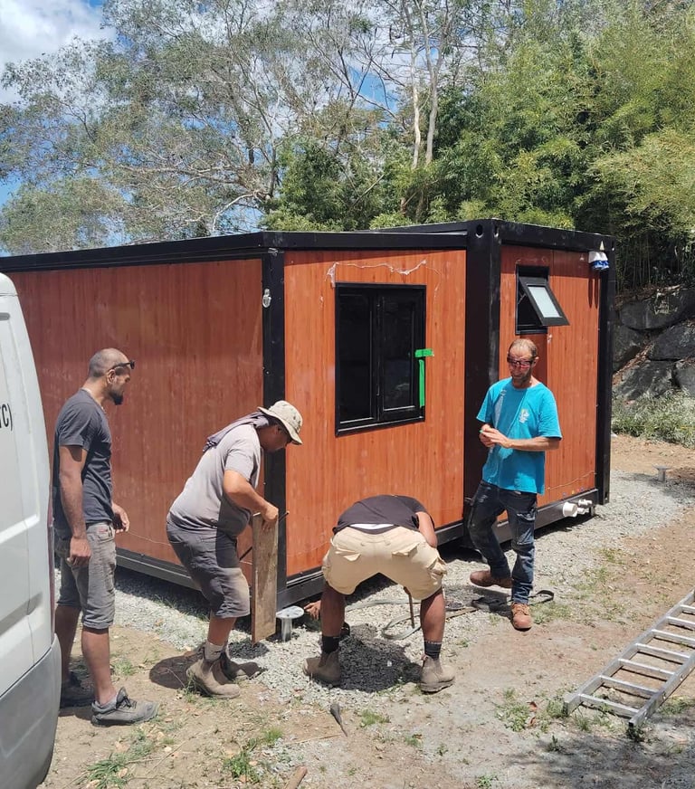 Ouvriers installant un conteneur habitable sur un terrain en gravier.
